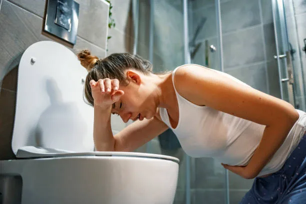 Young caucasian woman in toilet - pregnant, drunk or illness concept. Young dark-haired woman vomiting in toilet. Woman getting sick and vomiting over a toilet bowl kneeling down with her arms resting on the seat